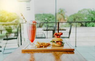 Delicious chicken burger with french fries and strawberry milkshake on restaurant table. Hamburger with french fries and strawberry milkshake on wooden table isolated photo