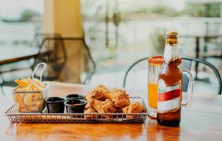 Traditional spicy chicken wings with fries and michelada accompanied with beer served on wooden table photo