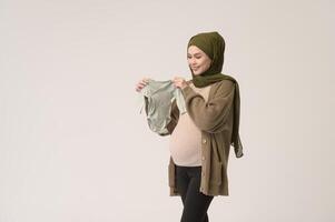 Portrait of Pregnant muslim woman in hijab holding baby cloth over white background studio photo