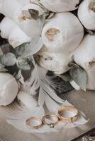 A bouquet of white flowers with a feather and three gold wedding rings photo