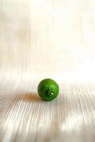 Single Green Lemon on White Cloth Tabletop photo