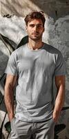 Man Wearing Grey T-Shirt and Pants Posing Against Wall photo