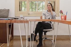 Smiling woman sitting at a large desk talking on a cell phone. photo