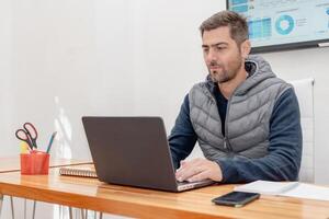 Serious and handsome man working on laptop sitting at his desk. photo