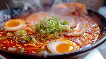 A close-up of a steaming bowl of spicy ramen noodle soup, with visible slices of tender pork, boiled egg halves, and fresh green onions, all surrounded by a rich, red broth photo