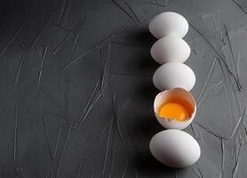 Row of white eggs and single broken egg with a yolk photo