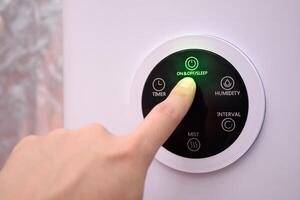 Close up of hand pressing on the digital on and off button of a smart humidifier in a smart home or green house. photo