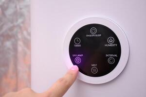 Close up hand pressing digital UV lamp button on smart humidifier in green house and smart home. photo