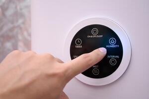 Close up man hand pressing the digital humidifier button on a smart humidifier in a smart home or green house. photo