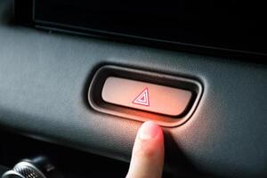 Finger pressing the emergency light button on a car to symbolize a car accident along with a red light on the control panel button. photo