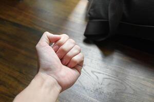 Fist of hand on desk soft sunlight and work bag background,hands on the table, hands conveying anger,hands showing determination,pressure at work,wood pattern work table,black work bag. photo