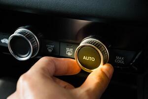Hand turning the button to automatically adjust the air conditioning temperature in a modenrn car luxury interior with yellow light in a 2024. photo