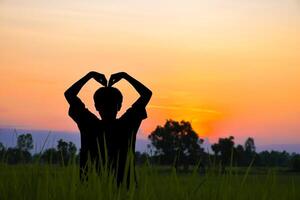 Silhouette of a man making a heart shape with his hands in beautiful rice fields and sunset atmosphere in the evening. photo