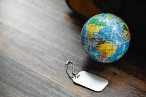 Earth Globe and Dog Tag on wood pattern work desk and soft sunlight background,Dog Tag empty,World and map of Americas,Top view with copy space,Desktop equipment,Concept of Travel and Work,Earth map. photo