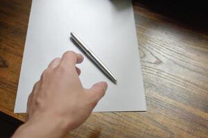 Hand with pen over blank paper on wooden work desk beautiful pattern,Hand reaching for pen,concept of idea and actions, Work equipment in workplace,Hand close-up with pen and paper,note idea for work. photo