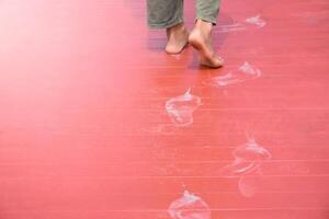 Man feet walking and white footprints on red wood floor in soft sunlight blurred background for concept of dirty marks and theft. photo