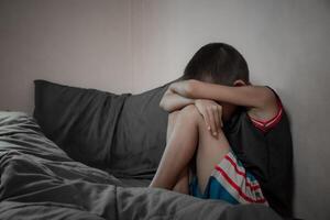 Side view of a boy sitting on a bed scared and unhappy from depression due to family problems in dark tone background. Children who are depressed and suffering from domestic violence. photo