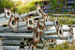 Rusty metal utility poles piled up on top of each other at the deserted area used for construction work or traffic lights to provide brightness in old storage area and forest background. photo