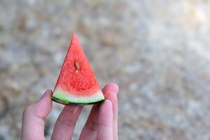 Hand holding watermelon cut into triangular pieces close-up in stone pattern floor and sunlight blurred background for design and health fruit concept. photo