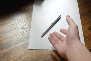 Hand with pen over blank paper on wooden work desk beautiful pattern,Hand reaching for pen,concept of idea and actions, Work equipment in workplace,Hand close-up with pen and paper,note idea for work. photo