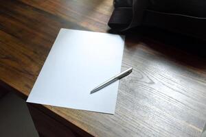 Pen and blank paper and work bag placed on a wooden patterned work desk in soft sunlight background for concept of office and take note. photo