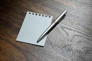 Close-up silver pen and blank paper of notebook on wooden pattern desk at office for taking notes and designing. photo