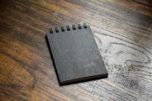 Small black notebook sits on a wooden patterned desk for taking notes or writing. photo