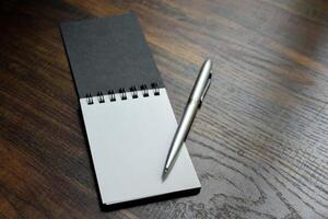 Silver pen and blank paper of notebook placed on wooden pattern desk at office for design ideas and taking notes. photo