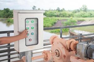 Hand with Control electrical systems and Machine motor on background dams and nature,Hand pressing on electrical distribution control box,Distribute electrical power steam on water surface and sky. photo