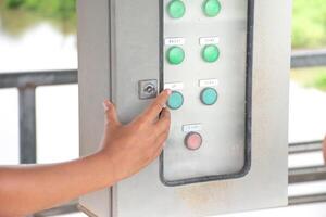 Hand with Control electrical systems and Machine motor on background dams and nature,Hand pressing on electrical distribution control box,Distribute electrical power steam on water surface and sky. photo
