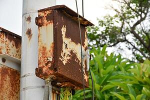 Broken and rusted electrical control box or electric Switchboard on electrical pole at outdoor park with forest and sky background. photo