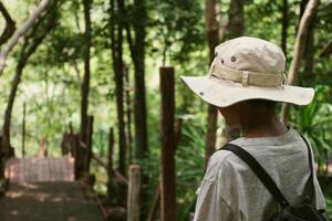 Close-up back of a man wearing a hiking hat and a bridge bag at the mountain forest in the blurred background. photo