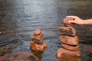 Hand holding stone and place the stones next to each other so that they are tall and balanced for zen stacked rocks in river flow. photo