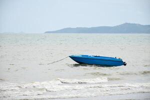 Blue speedboat is parked in the sea on a day with high waves and a storm and an overcast sky showing a rough environment with dusty air and murky water. photo