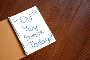 White notebook paper with the words Did You Smile Today written on paper for questions and speech concepts on a textured brown wooden background. photo