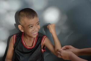 Asian boy smiling cheerfully with someone nursing a wound on his arm caused by an accident a view from above on a background of a gray wall and beautiful bokeh sunlight. photo