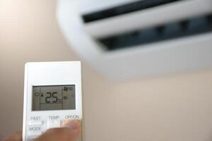 Hand holding remote control to turn on the air conditioner at 25 degrees celsius in white room and soft sunlight blurred background concept of save power and electrical appliances. photo