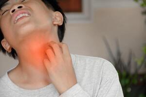 Asian young man touching his neck and showing a pained expression due to a sore throat or an itchy throat due to irritation caused by bacteria infection. photo