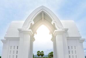 Beautiful white entrance arch architecture with Thai temple pattern with Indian pattern or a white Thai temple chapel with sunlight in the center on sky and forest background. photo