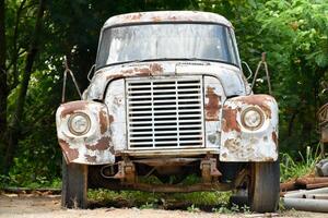 Abandoned classic truck and has rust font-view at old storage place in natural forest and scrap metal background for concept of cars and transportation. photo