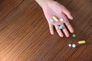 Many pills on hand and on wood pattern floor top-view different colored tablets and capsules indicate an overdose for concept of medicine and medical. photo