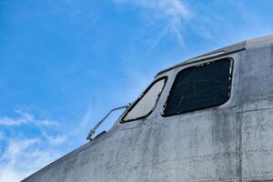 Close front outside view of the head of a silver old airplane showing the texture of steel and broken window glass on a blue sky background. photo