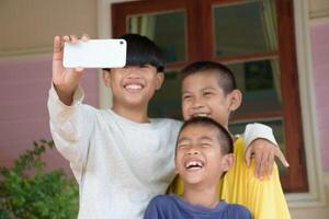 Close up of smartphone and a group of Asian boys taking group selfies against the background of outdoors and a green forest. Three boys smiling charmingly and taking pictures using smartphones. photo