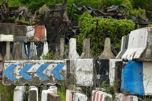 The storage area for old or disused items is filled with concrete barrier and many decayed and rusted steel frames in the background of a desolate forest. photo