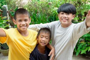 Three boys group together and playfully smiling taking selfie by smartphone camera and looking at camera on green forest outdoor background for holiday and group activity concept. photo