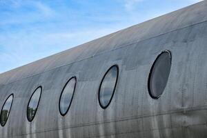 The body of the plane with circular windows shows a silver metallic surface of an idle airplane on the sky background. photo