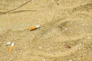 Close-up cigarette butts lie on the sand and shell fragments at the seaside causing a negative effect on the marine environment. photo
