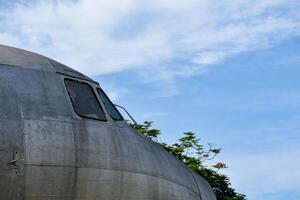 Old airplane head part and the cockpit and emergency door showing rusted steel surfaces and decorative glass windows on the background of the blue sky and forest photo