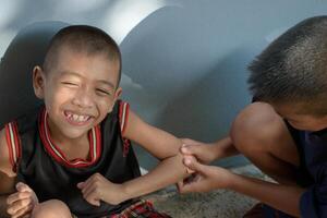 Top-view of two asian young boy smiling cheerfully sitting on the floor and getting treatment for a wound caused by an accident on a gray concrete background and beautiful bokeh lights. photo