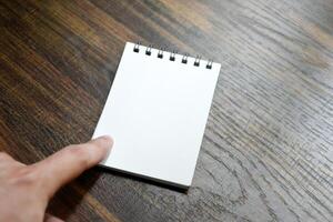 Hand pointing at blank white paper of notebook on wooden patterned desk background at office. photo